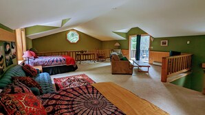 A cozy attic bedroom with a sloped ceiling, a large window, a bed, a sofa, a wooden bench, and a small table. - Big Mazama Cabin on 5 Acres: Huge Goat Wall Views (Mazama)