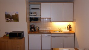 A compact kitchen with white cabinets, a microwave, a coffee maker, and a dishwasher.