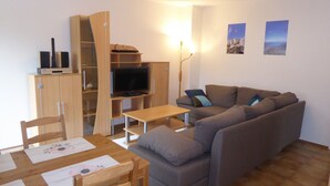 A living room with a sofa, a TV, a wooden cabinet, and a dining table.