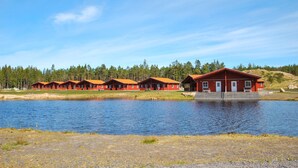 En rad röda stugor med en sjö i förgrunden och en skog i bakgrunden.