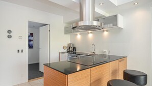 Et moderne køkken med en central ø, rustfrie hårde hvidevarer og træskabe.