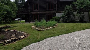 Eine Blockhütte mit einer großen Veranda, einem Schotterweg und einem gepflegten Rasen.