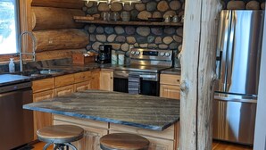 Eine rustikale Küche mit Steinwand, Holzbalken, einer großen Kochinsel mit Hockern und modernen Geräten.