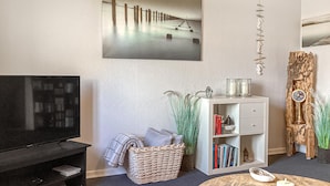 A living room with a flat-screen TV, a bookshelf, a wicker basket, and a round coffee table with candles. - Gorgeous apartment in Rødekro with WiFi (Rødekro)