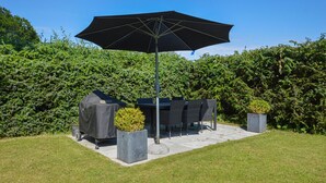 An outdoor patio with a table and chairs, a large umbrella, and a hedge in the background. - Gorgeous apartment in Rødekro with WiFi (Rødekro)