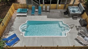 Une piscine rectangulaire avec un escalier, entourée d’une clôture en bois, et équipée de chaises longues et d’un jacuzzi.