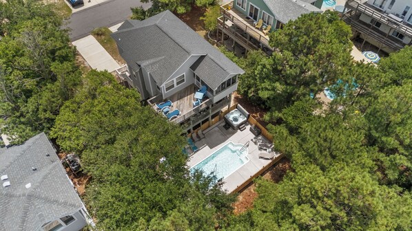 Une maison à deux étages avec une piscine dans le jardin, entourée d’arbres denses.