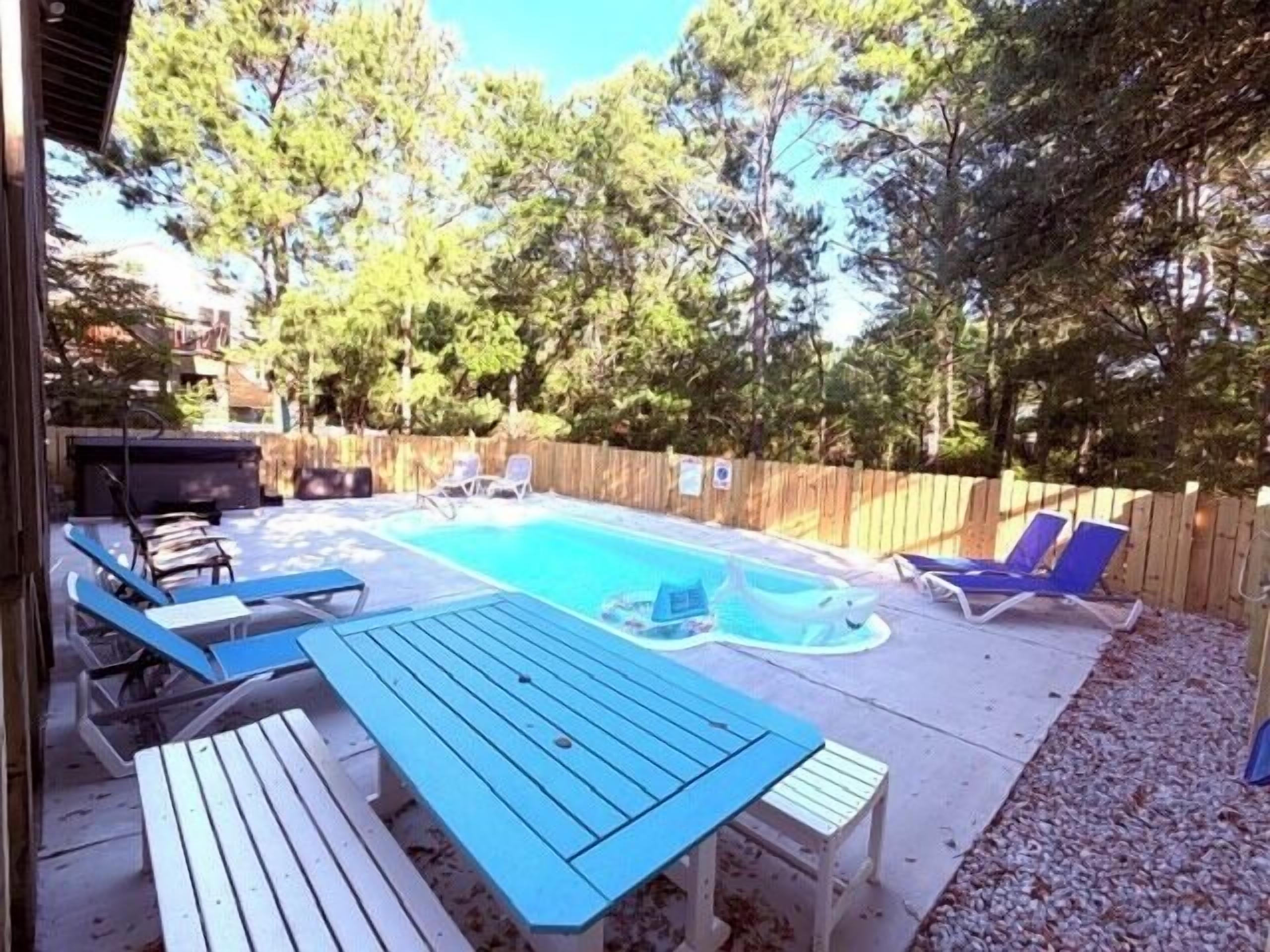 Un patio trasero con piscina, sillas de descanso y una mesa de picnic.