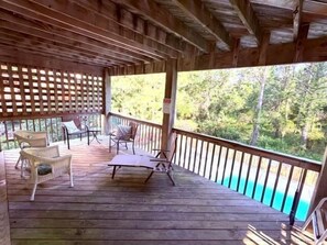 A wooden deck with outdoor furniture, a pool, and a forested backdrop.