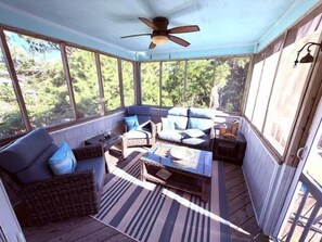 A screened porch with wicker furniture, a ceiling fan, and a view of the outdoors.