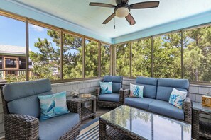 A sunroom with wicker furniture, large windows, and a ceiling fan.