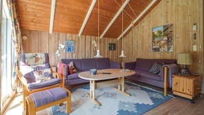 A cozy room with wooden walls and ceiling, a purple sofa, a small round table, and a lamp on a wooden cabinet.