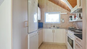 A compact kitchen with a refrigerator, stove, sink, and wooden cabinets.