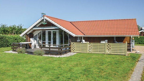 A house with a red-tiled roof, a covered porch with outdoor seating, and a fenced garden area.