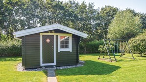 A small shed with a door and window, surrounded by a grassy yard and a swing set.