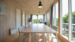 Una larga mesa de comedor con sillas, un televisor y un sofá en una habitación con paredes de madera y ventanas grandes.