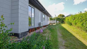 Una casa moderna con fachada gris, ventanas amplias y un jardín bien cuidado con diversas plantas y flores.