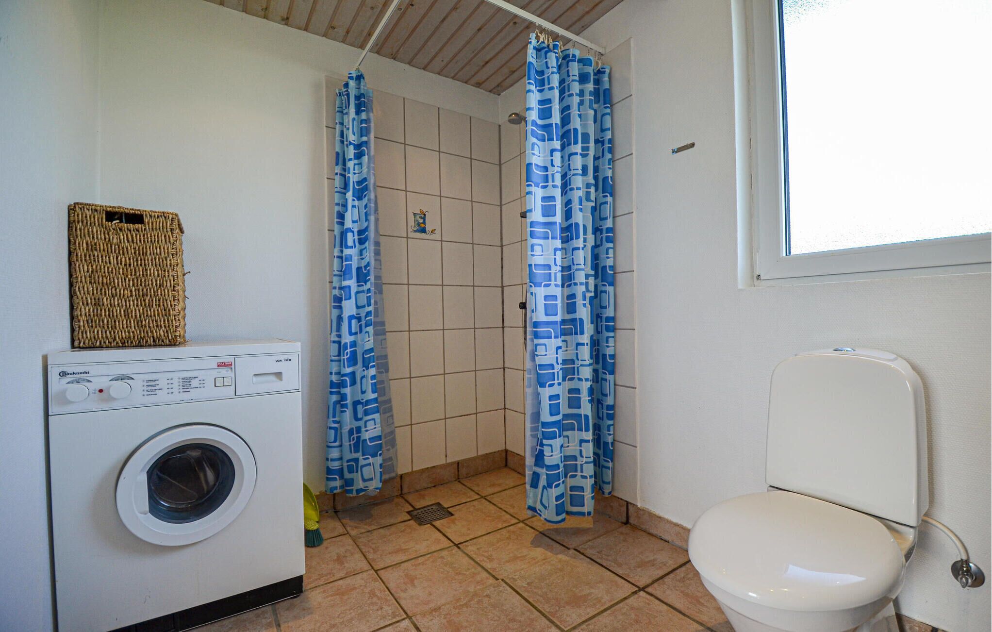 Un baño compacto con lavadora, inodoro y zona de ducha con cortinas azules estampadas.