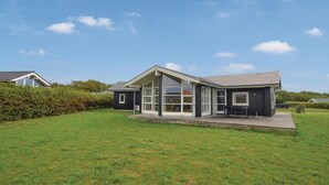 A modern house with a large glass front, a covered patio, and a well-maintained lawn.