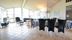 A spacious living area with a high ceiling, a dining table set with chairs, a sofa, and a television.