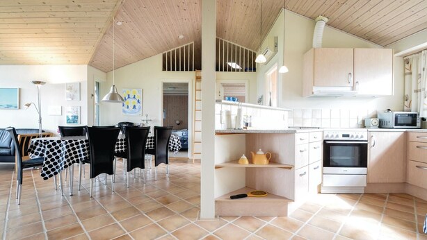 A modern kitchen with white cabinets, a stove, and a microwave. There is a dining area with a table and chairs.