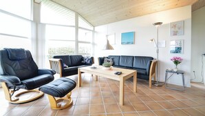 A spacious living room with a black leather sofa, a black leather chair, a wooden coffee table, and a floor lamp.