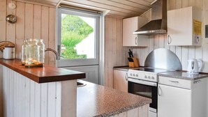 A compact kitchen with wooden cabinets, a stainless steel range hood, a built-in oven, and a window with a view of greenery.
