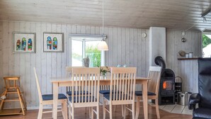 A cozy room with a wooden table and chairs, a hanging light fixture, a fireplace, and two framed artworks on the wall.