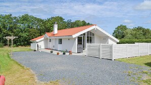A single-story white house with a red-tiled roof, a gravel driveway, and a white fence.
