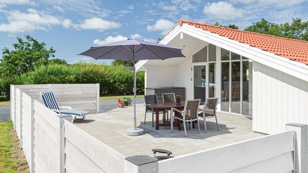 A covered patio with a table and chairs, a grill, and a lounge chair.