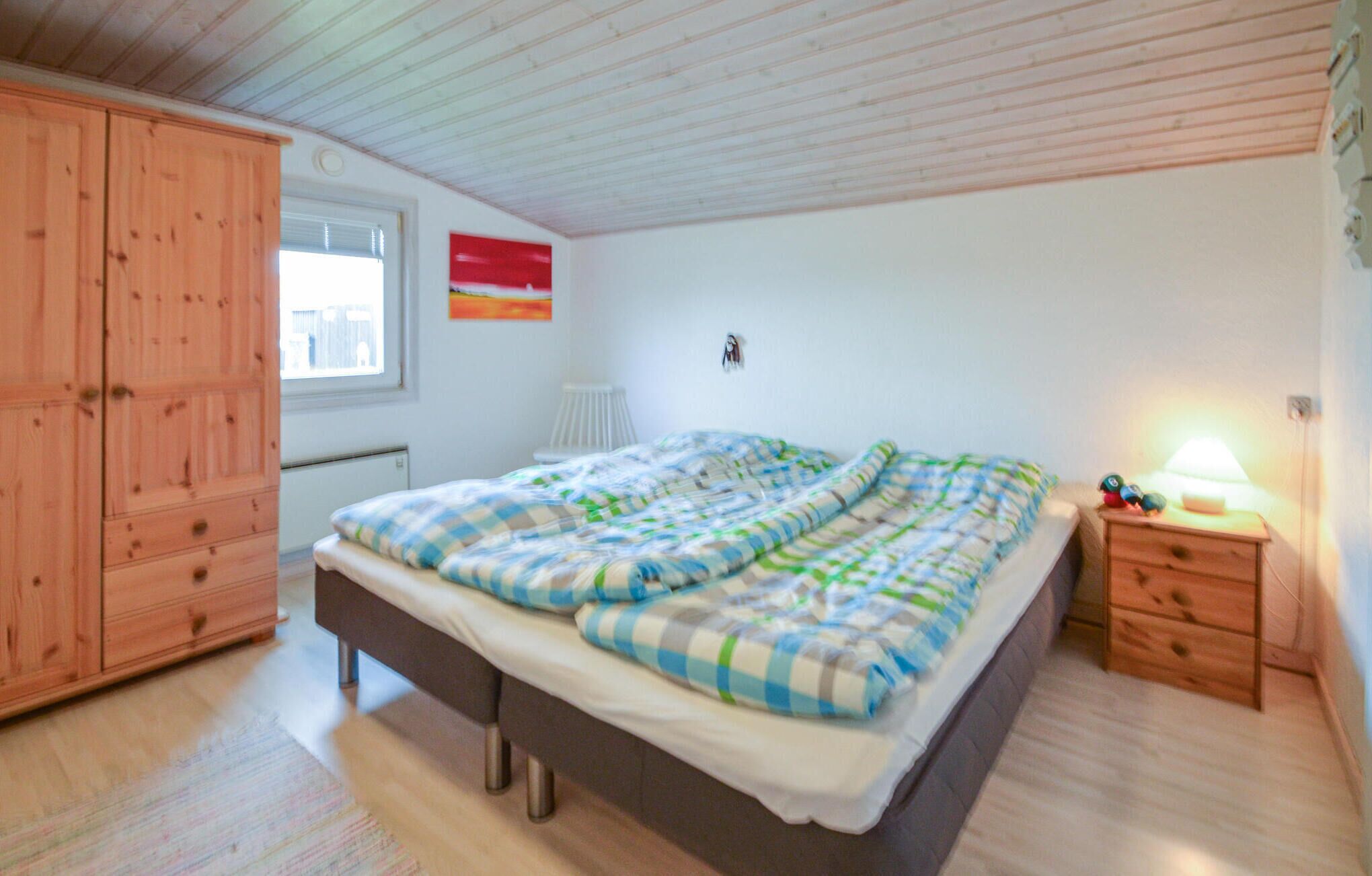 Quarto com cama, guarda-roupa de madeira e mesa de cabeceira com luminária.
