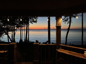 Una terraza de madera con vista al mar al atardecer, con barandilla y un banco.