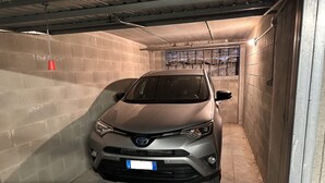 Un coche estacionado en un garaje estrecho y cerrado, con paredes de hormigón y techo de metal.