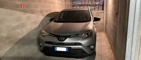 A car parked in a narrow, enclosed garage with concrete walls and a metal roof.