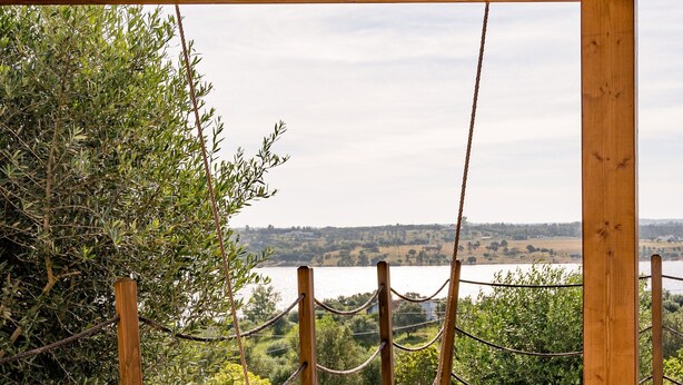 A wooden deck with a swing, overlooking a body of water and greenery.