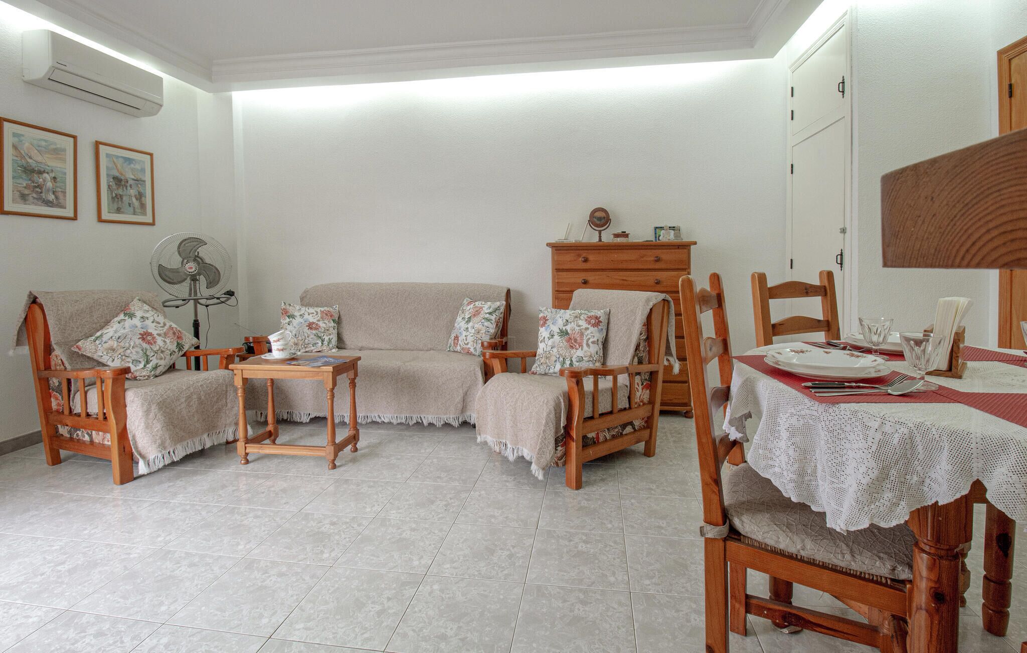 A cozy living room with a sofa, two armchairs, a wooden table set for dining, and a wooden cabinet.