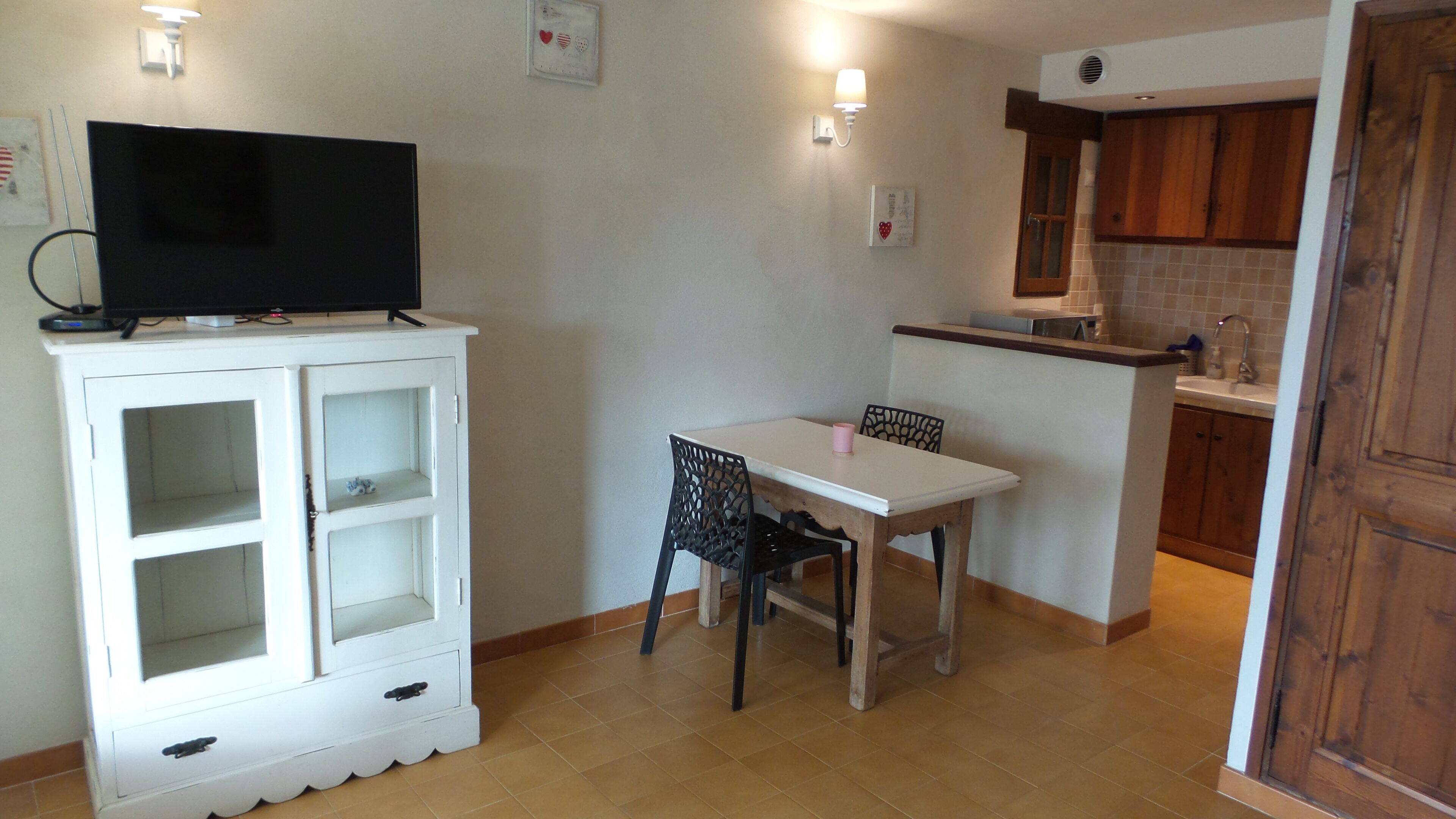 A small kitchen with a dining table, chairs, a TV on a cabinet, and wooden cabinets.