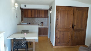 A compact kitchen with wooden cabinets, a white countertop, and a dining area with a chair. - Studio with private garden in Sanary (Sanary-sur-Mer)