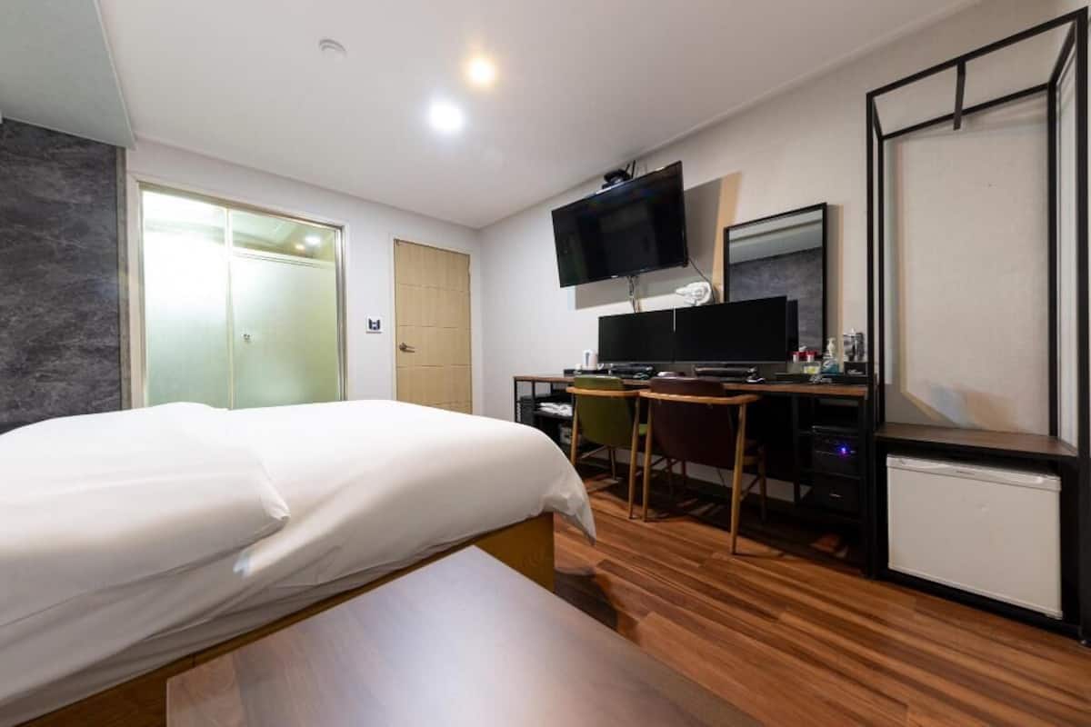 A hotel room with a bed, a desk with a computer, a television, and a mini-fridge.