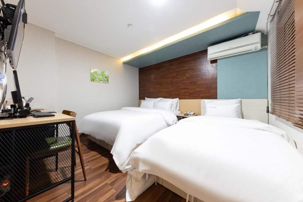 A hotel room with two beds, a desk with a computer, and an air conditioning unit.