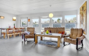 A spacious living room with a large window, a dining area with wooden furniture, and a cozy seating area with striped chairs. - Beautiful home in Hals with kitchen (Hals)