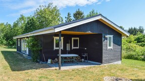 En liten, mörk trästuga med en inglasad veranda, ett bord och en stol.