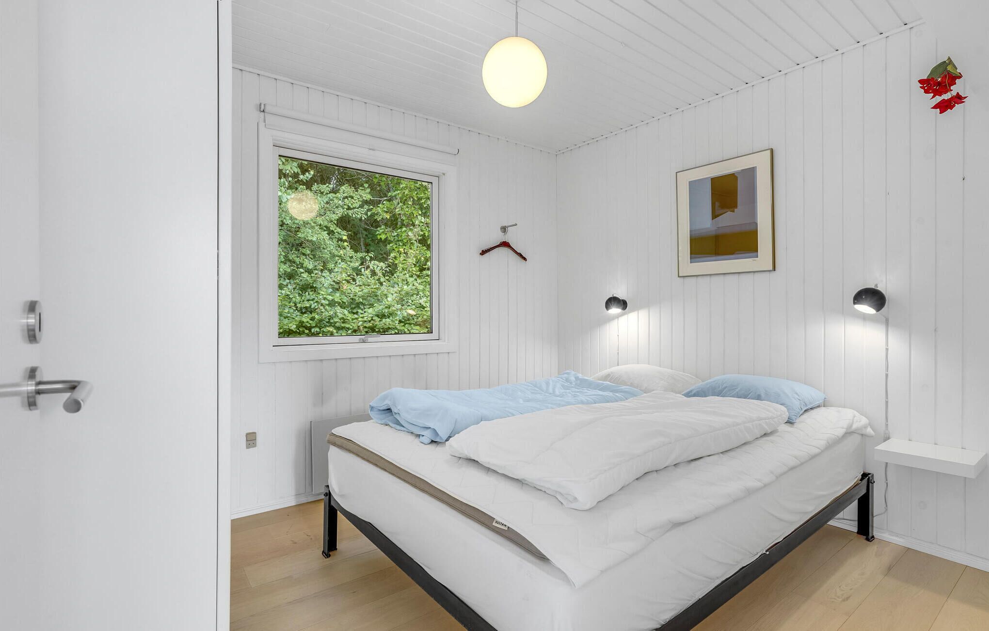 A bedroom with a bed, a window, a wall-mounted light, and a picture frame.