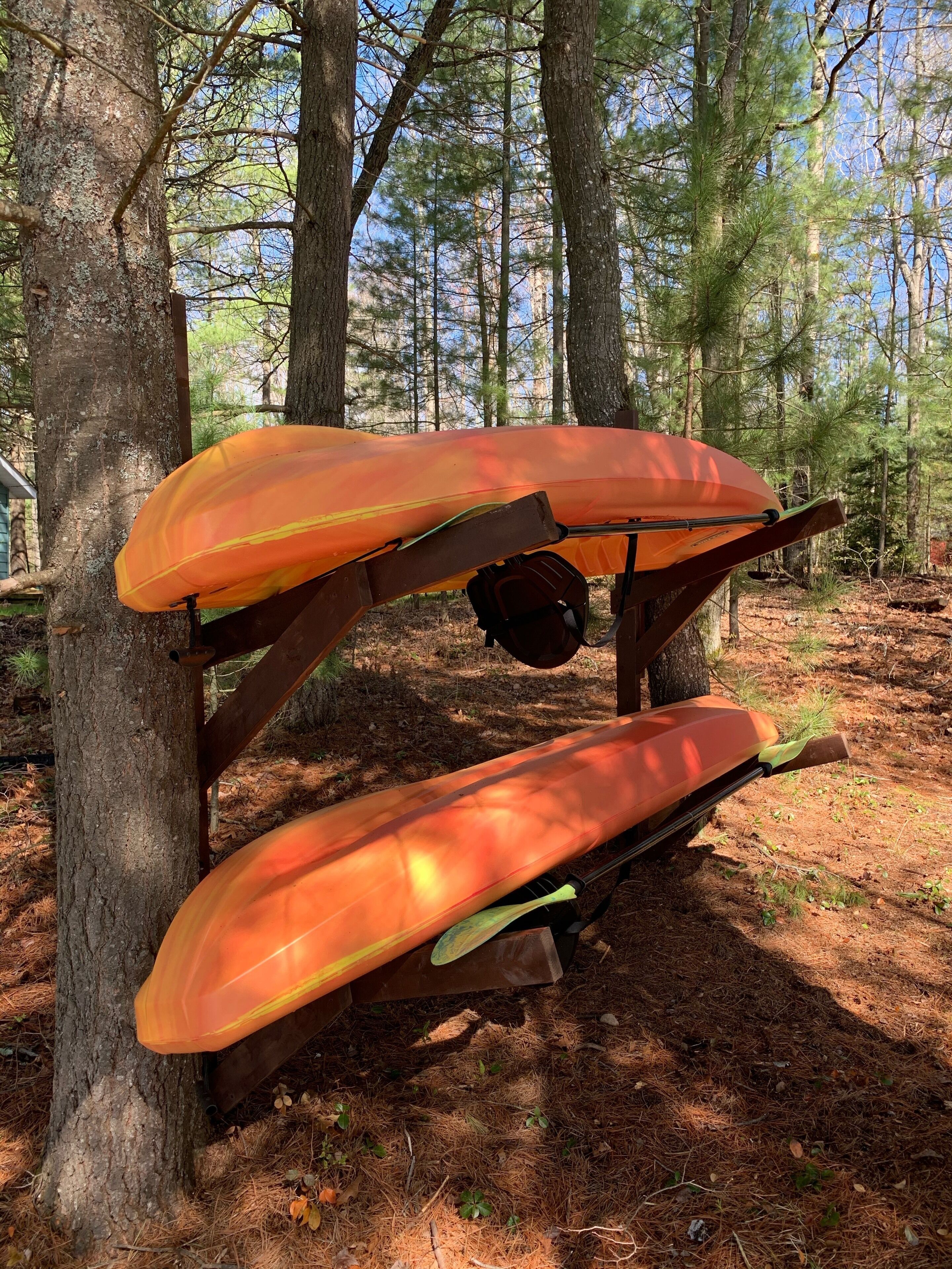 A wooden structure with two orange kayaks mounted on it, set in a forested area.