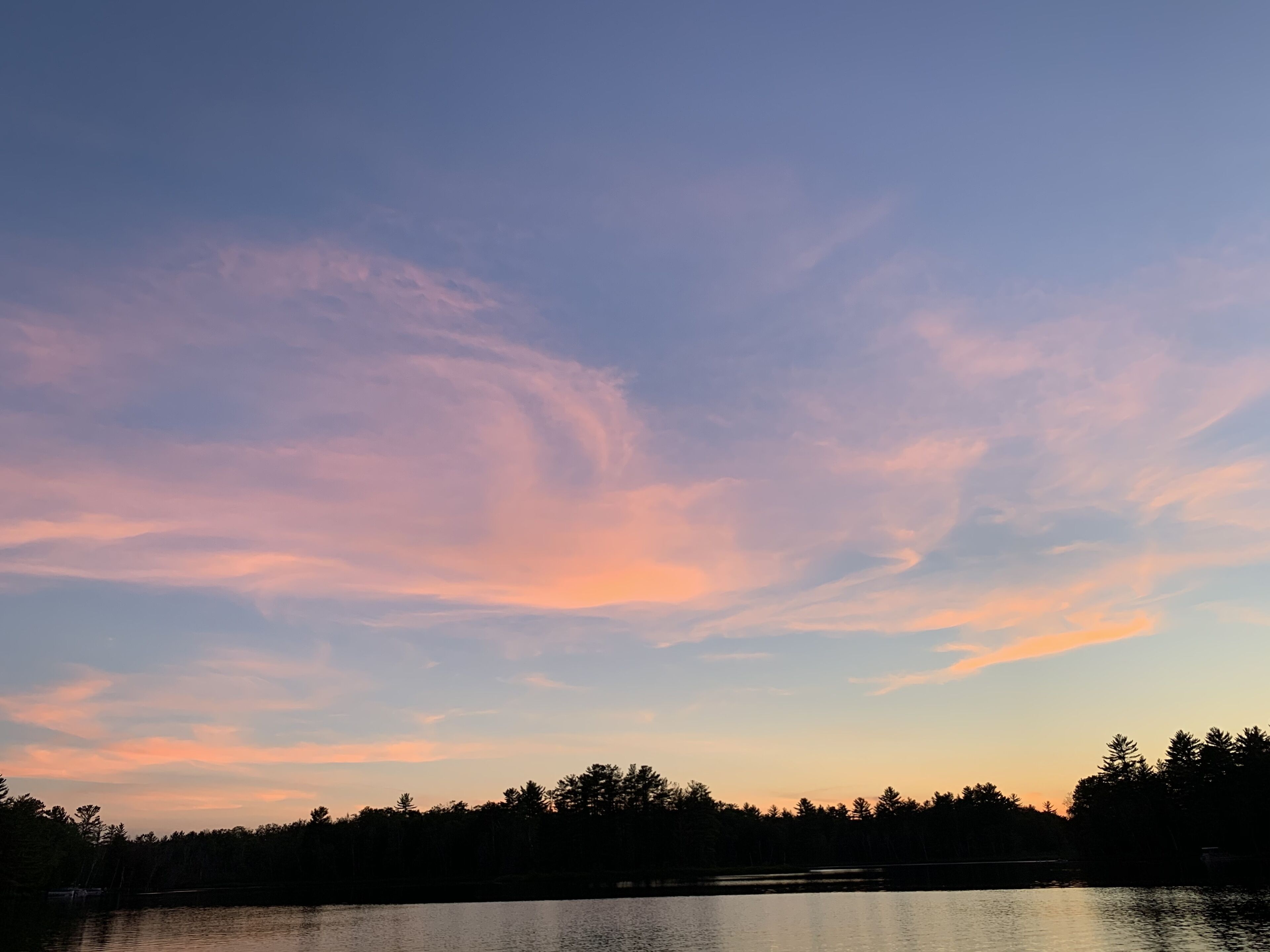 A calm lake at dusk with a clear sky and silhouettes of trees in the background.