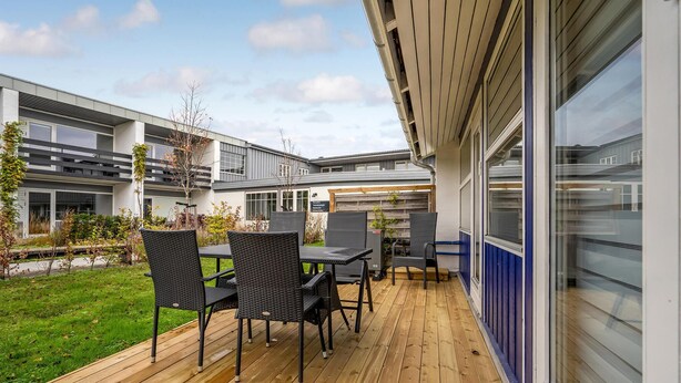 Ein moderner Außenbereich mit Terrasse, Holzboden, schwarzer Rattanmöbeln und Blick auf angrenzende Gebäude.