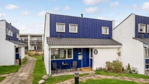Ein modernes, zweistöckiges Haus mit blauer Fassade und weißem Zierrat, mit einer kleinen Veranda, einer Bank und einer Tür, auf der die Nummer 50 steht.