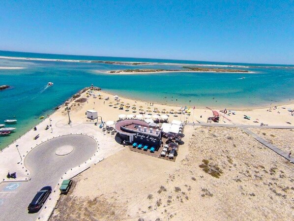 Relax on the beach with a drink at the central bar surrounded by lounge chairs and umbrellas.