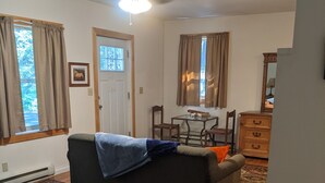 A room with a ceiling fan, a sofa, a dining table with chairs, a dresser, and a door. - Cozy Mazama Studio on 5 Acres-Trail Access & Views (Mazama)