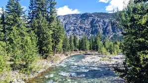 A river flowing through a forest with a rocky mountain in the background. - Cozy Mazama Studio on 5 Acres-Trail Access & Views (Mazama)